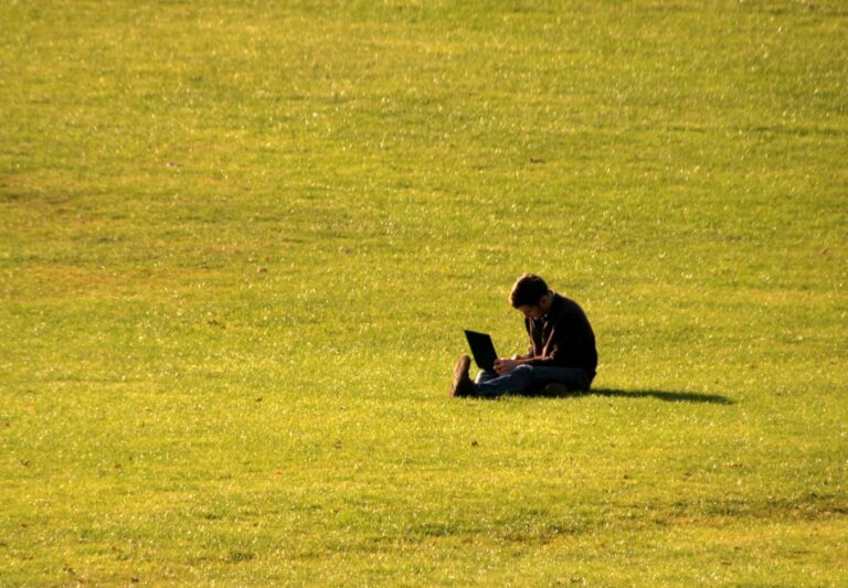 Sedící muž na trávě s notebookem